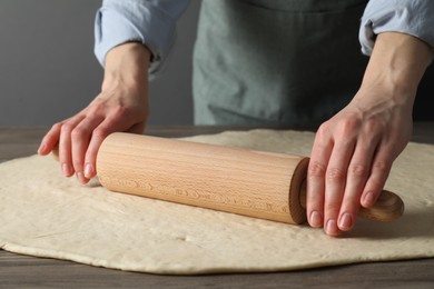 Woman rolling raw dough at wooden table, closeup