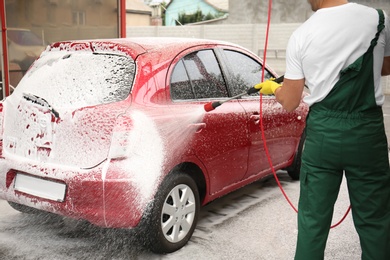 Male worker cleaning vehicle with high pressure foam jet at car wash