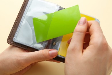 Woman holding business card holder with colorful cards on light yellow background, closeup