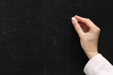 Photo of Teacher writing with chalk on black chalkboard, closeup. Space for text