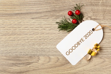 Tag with text Goodbye 2020 and festive decor on wooden table, flat lay. Space for text