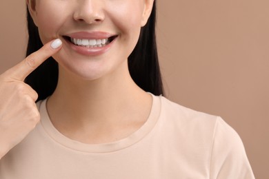 Woman showing her clean teeth and smiling on beige background, closeup