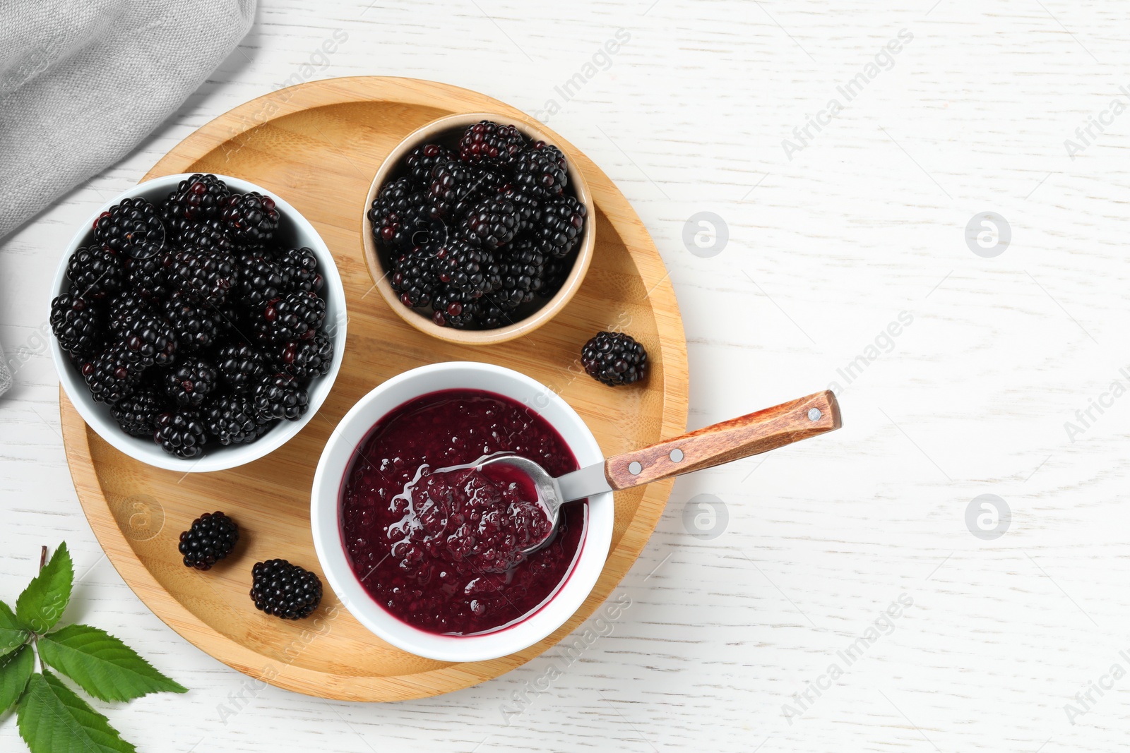 Photo of Fresh ripe blackberries and tasty jam on white wooden table, flat lay. Space for text