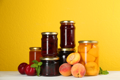 Jars of pickled fruits and jams on white wooden table