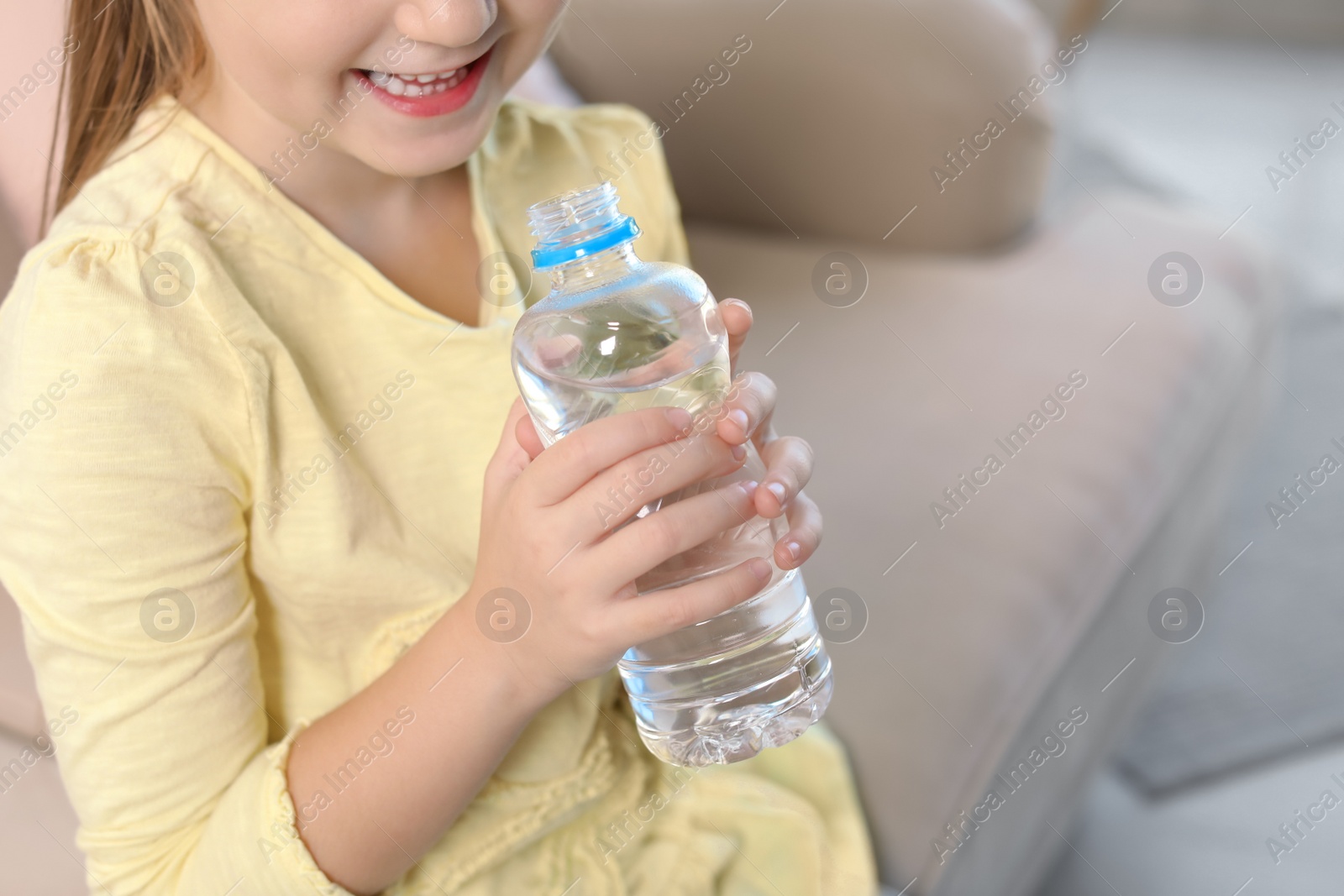 Photo of Cute little girl holding bottle with water indoors