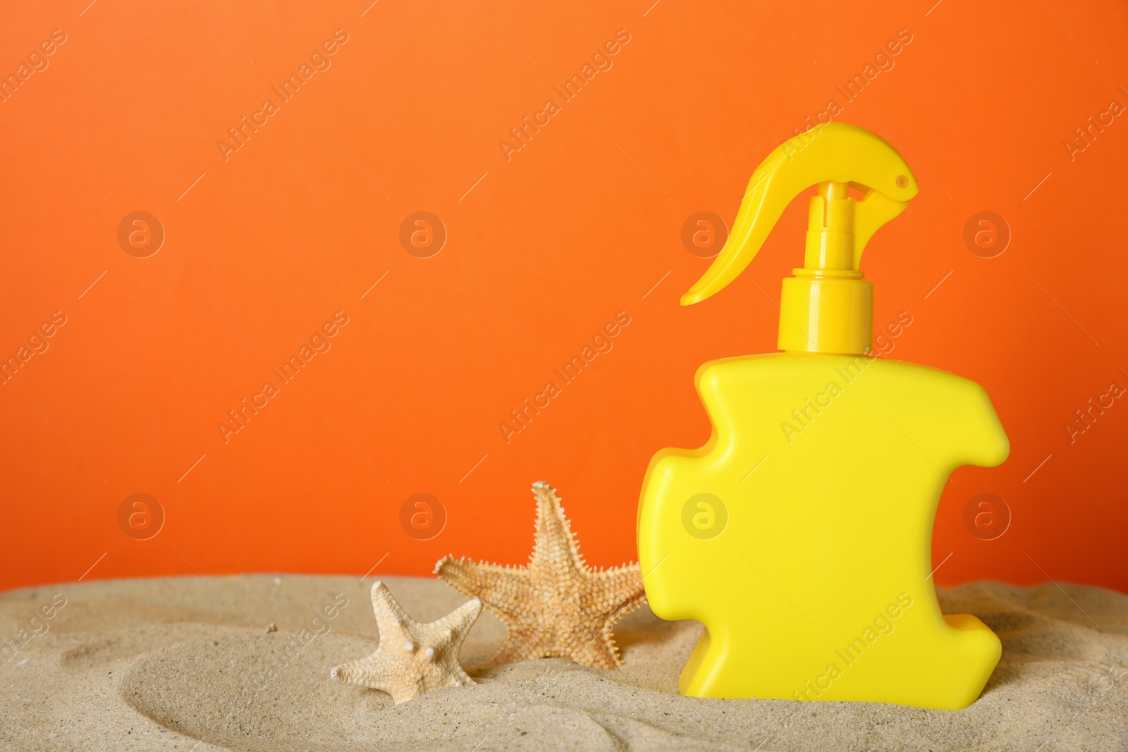 Photo of Suntan product and starfishes on sand against orange background. Space for text