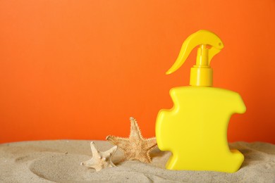 Suntan product and starfishes on sand against orange background. Space for text