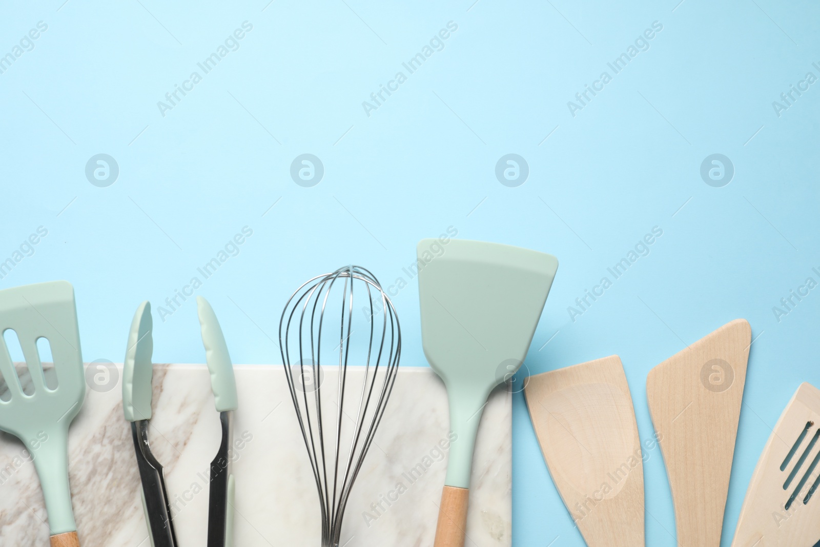 Photo of Different spatulas, whisk and tongs on light blue background, flat lay. Space for text