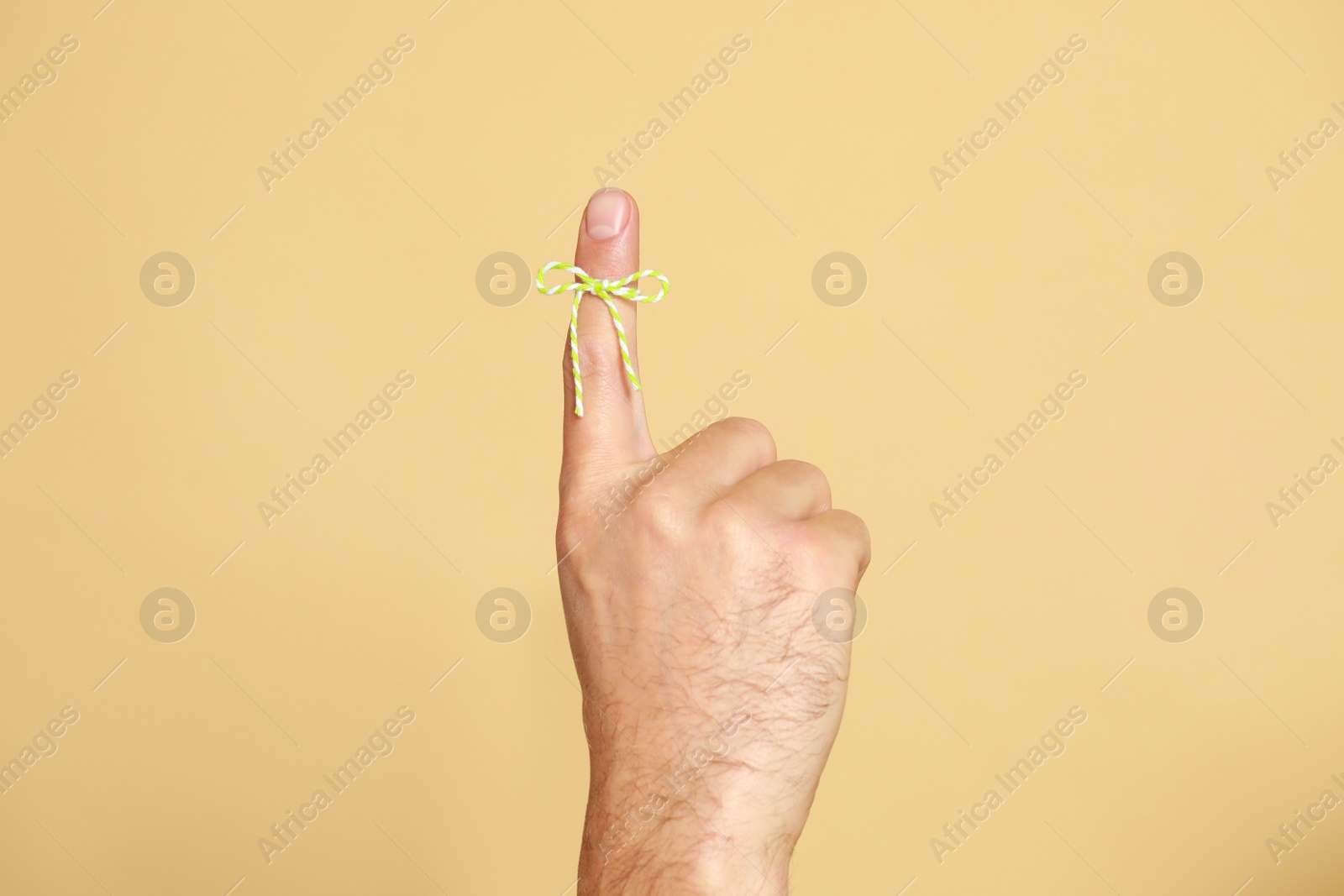 Photo of Man showing index finger with tied bow as reminder on beige background, closeup