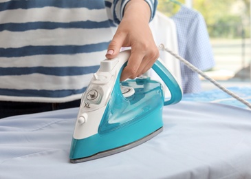 Woman ironing clothes on board indoors, closeup