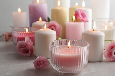 Burning candles and flowers on light grey table