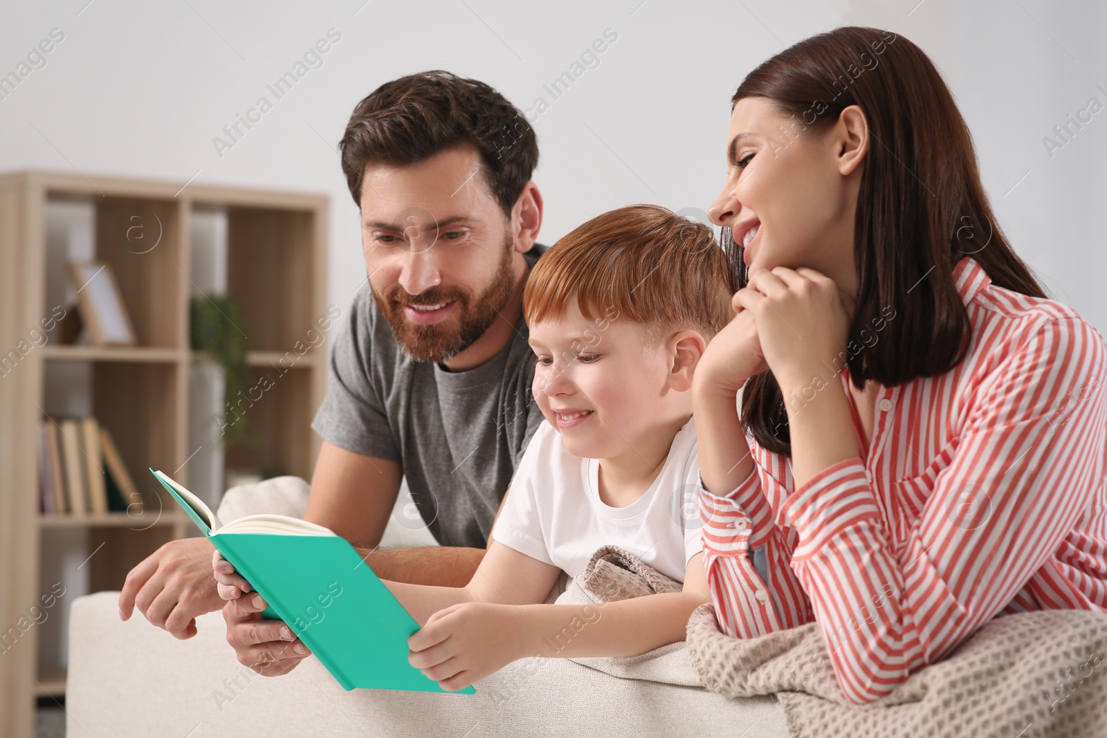 Photo of Happy parents with their child reading book on couch at home