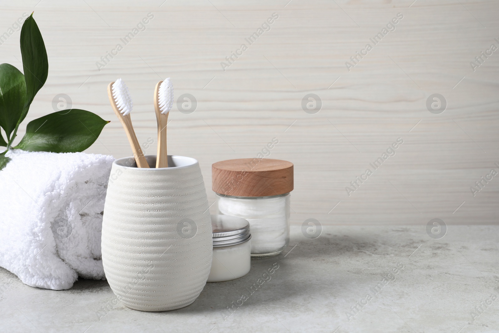 Photo of Bamboo toothbrushes in holder, towel, cotton pads and cream on light grey table, space for text