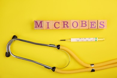 Photo of Word Microbes made with wooden cubes, syringe and stethoscope on yellow background, top view