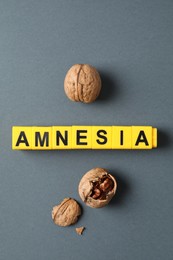Photo of Word Amnesia made of yellow cubes and walnuts on grey background, flat lay