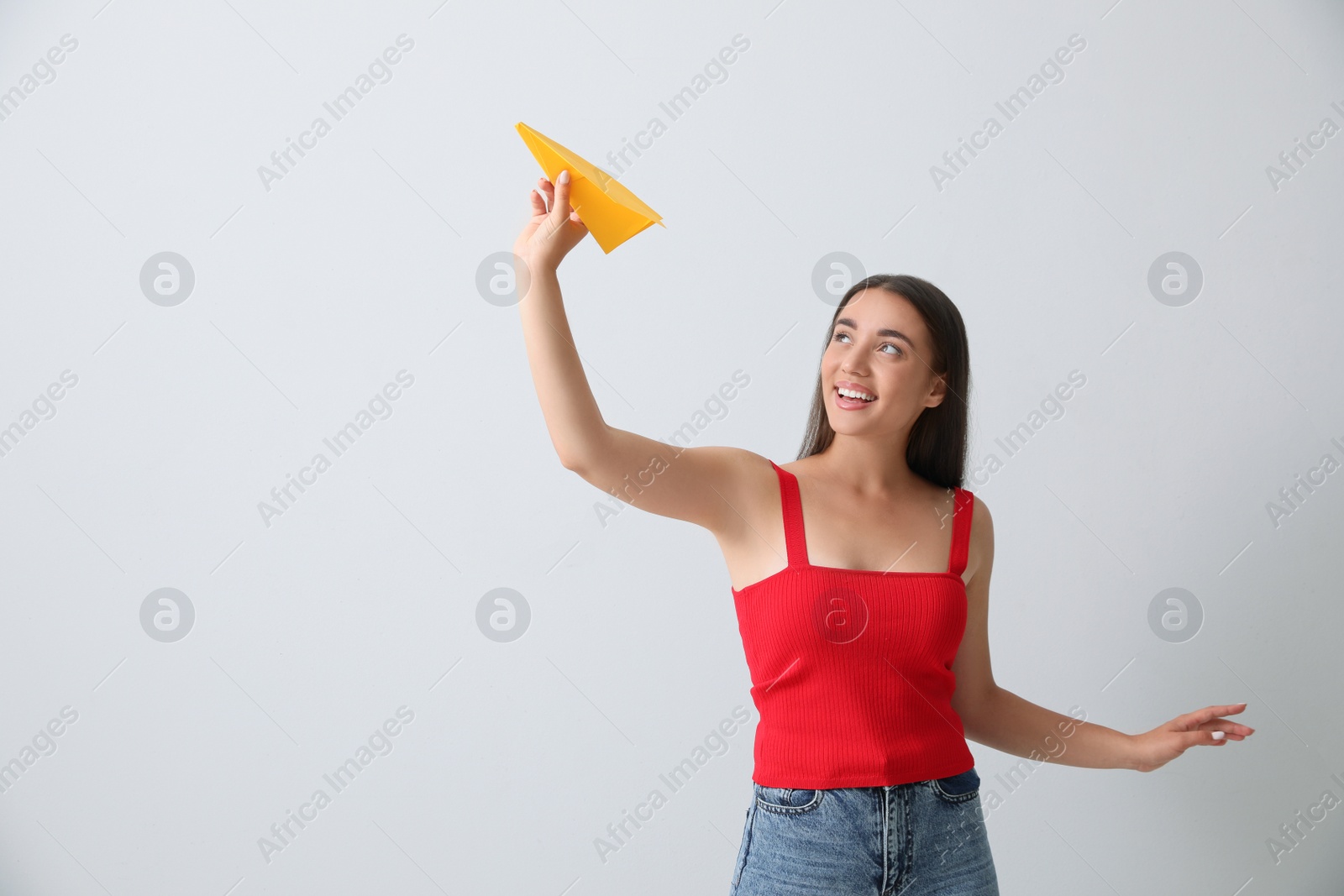 Photo of Beautiful young woman playing with paper plane on light grey background. Space for text