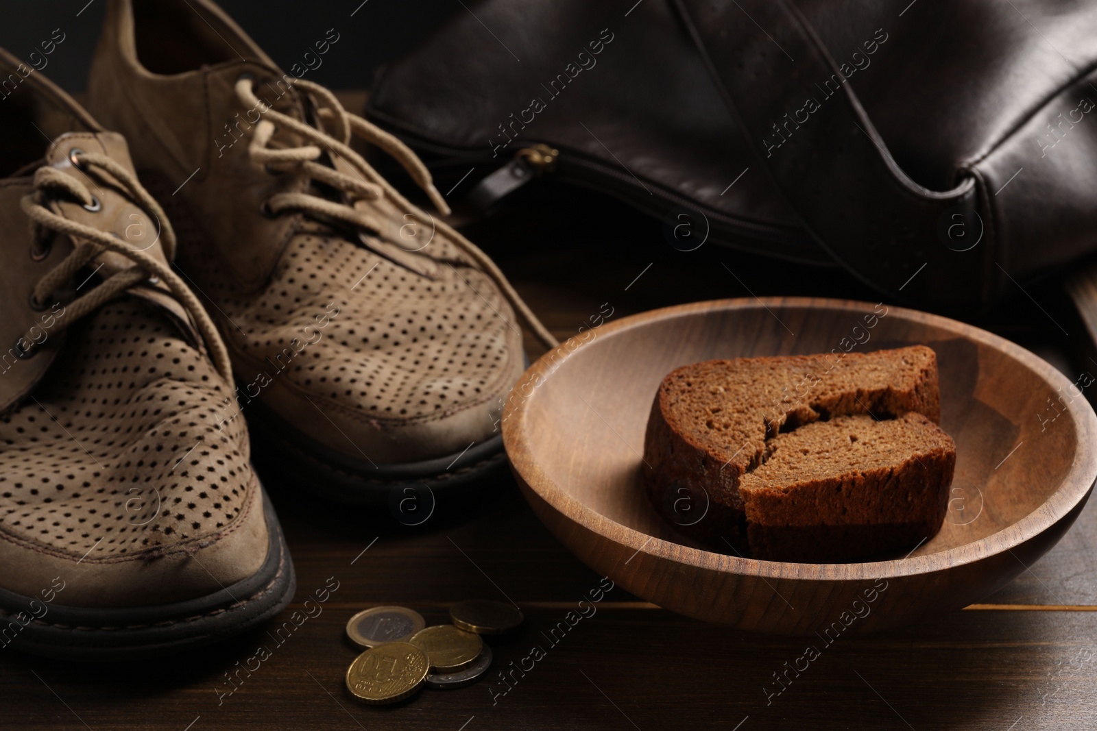 Photo of Poverty. Old shoes, bag, pieces of bread and coins on wooden table