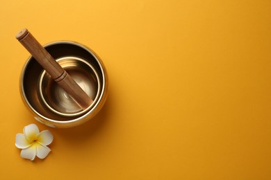Photo of Golden singing bowls, mallet and flower on orange background, flat lay. Space for text
