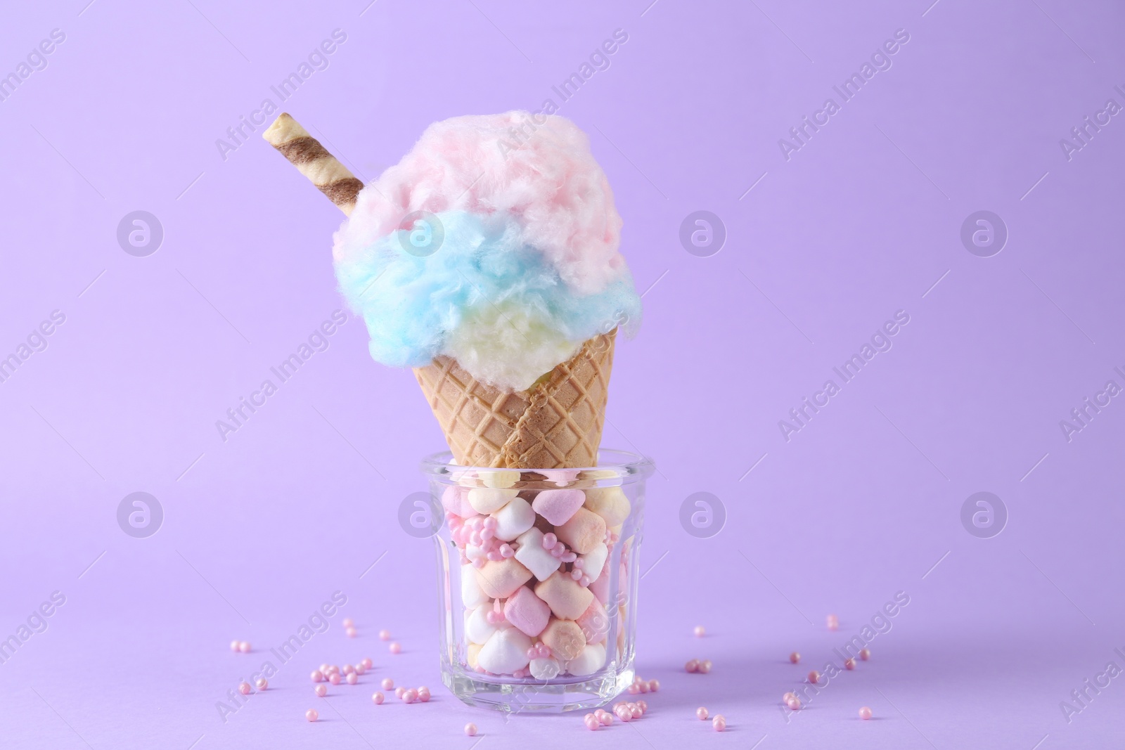 Photo of Sweet cotton candy in waffle cone on purple background, closeup