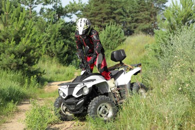 Photo of Man driving modern quad bike on sandy road near forest. Extreme sport