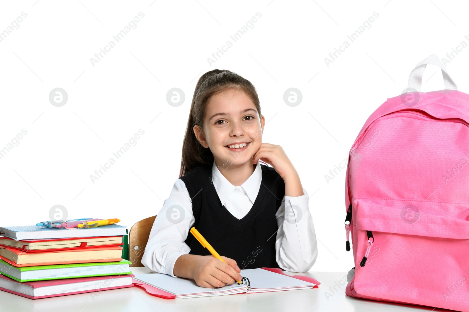 Photo of Little girl in uniform doing assignment at desk against white background. School stationery