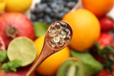 Vitamin pills in spoon over fresh fruits, top view