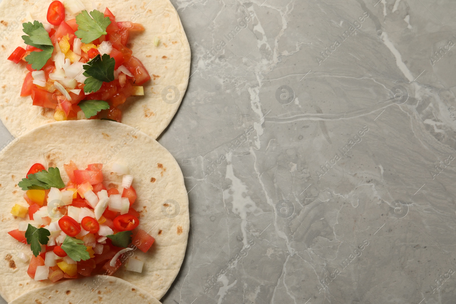 Photo of Delicious tacos with vegetables and parsley on grey marble table, top view. Space for text