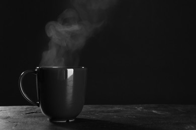 Cup with steam on table against black background. Space for text