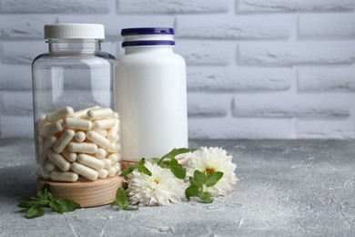 Medical bottles with pills and white flowers on light gray textured table, space for text