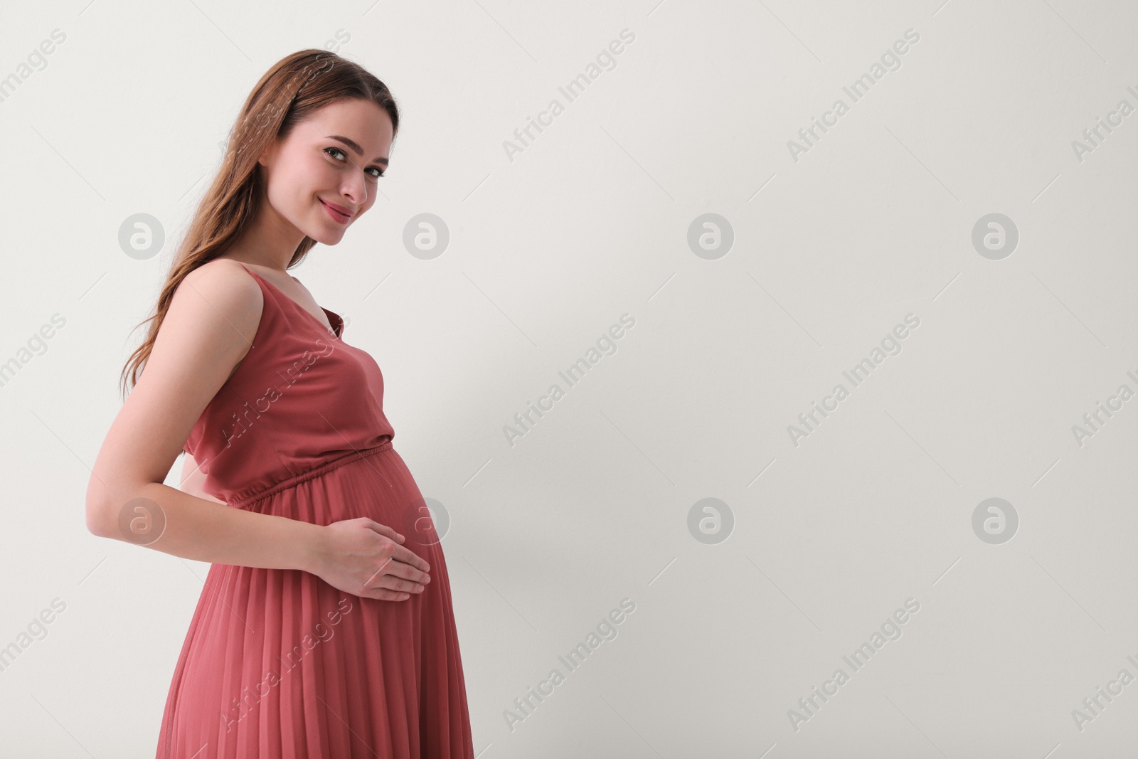 Photo of Beautiful young pregnant woman on light background. Space for text