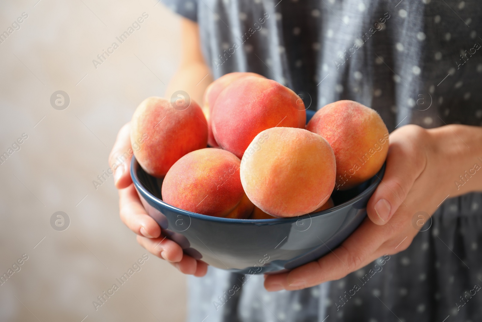 Photo of Woman holding bowl with delicious ripe peaches, closeup