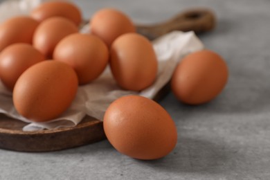 Chicken eggs, wooden board and parchment paper on grey table, closeup