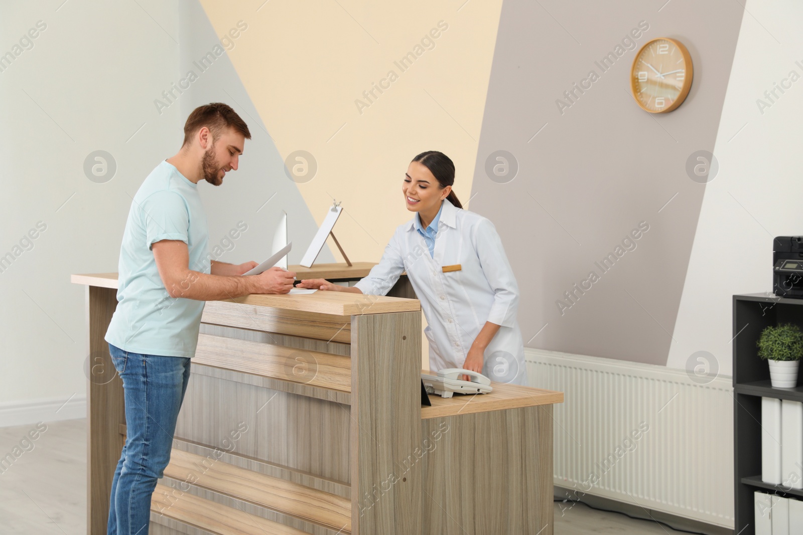Photo of Professional receptionist working with patient at desk in modern clinic