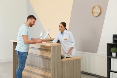 Professional receptionist working with patient at desk in modern clinic