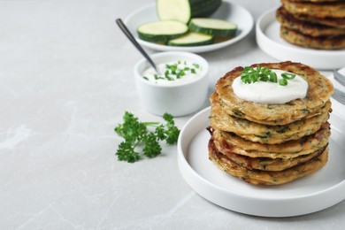 Photo of Delicious zucchini pancakes with sour cream served on light grey table. Space for text