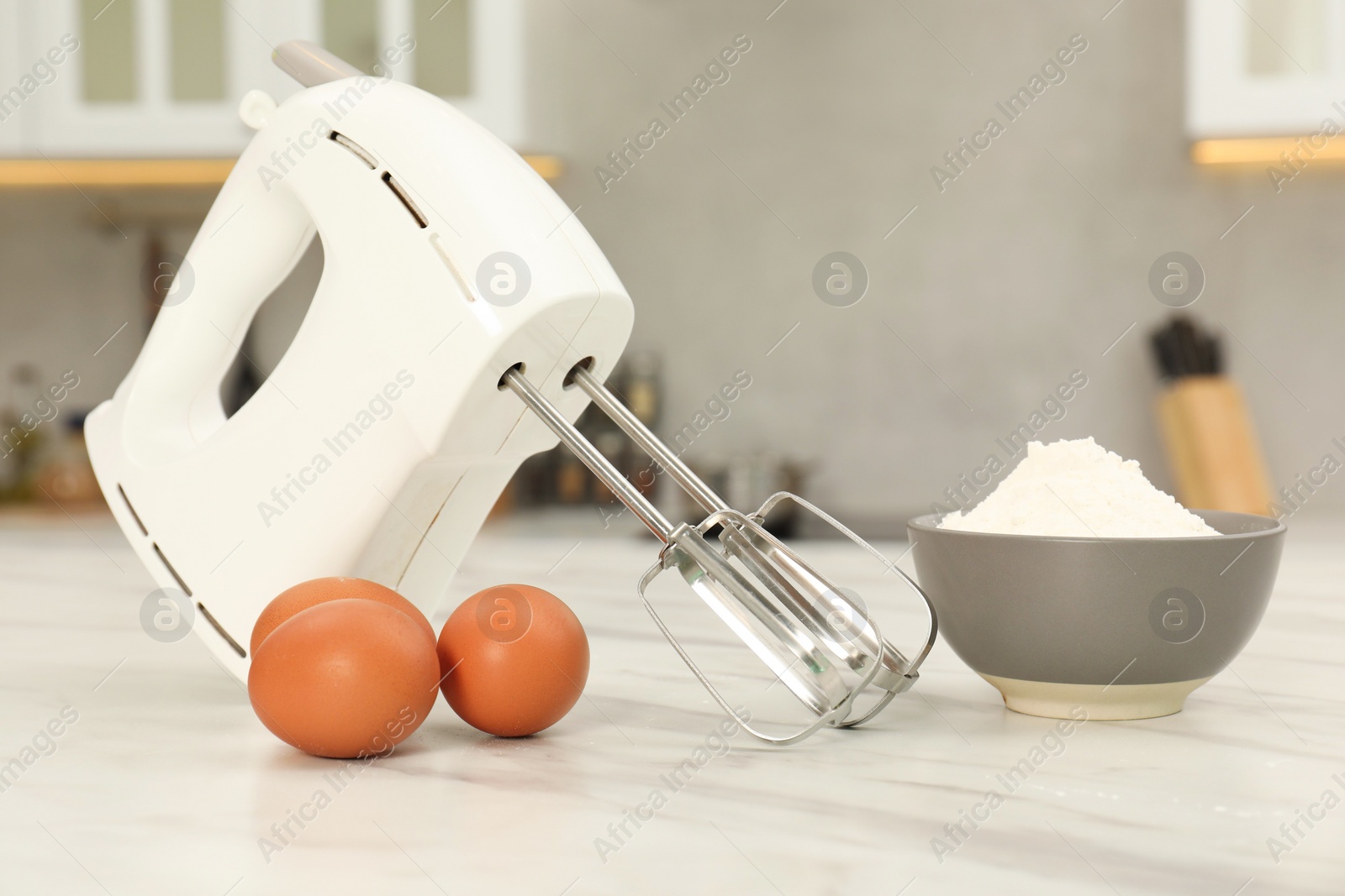 Photo of Modern mixer, eggs and bowl with flour on white marble table in kitchen