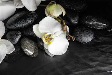 Stones and orchid flowers in water on black background. Zen lifestyle