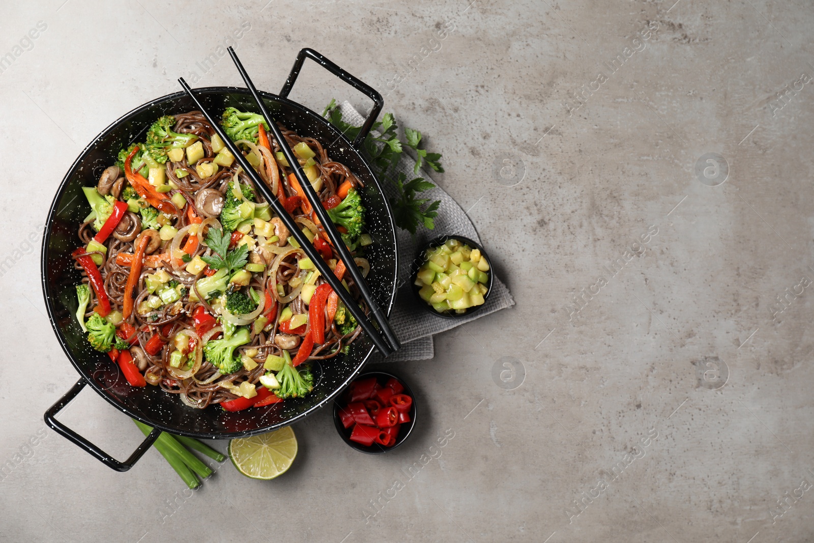 Photo of Stir-fry. Tasty noodles with meat in wok, chopsticks and ingredients on grey textured table, flat lay. Space for text