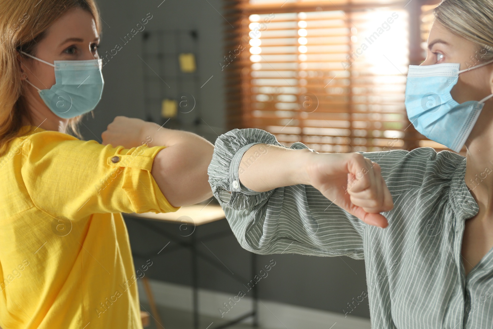 Photo of People greeting each other by bumping elbows instead of handshake indoors, closeup