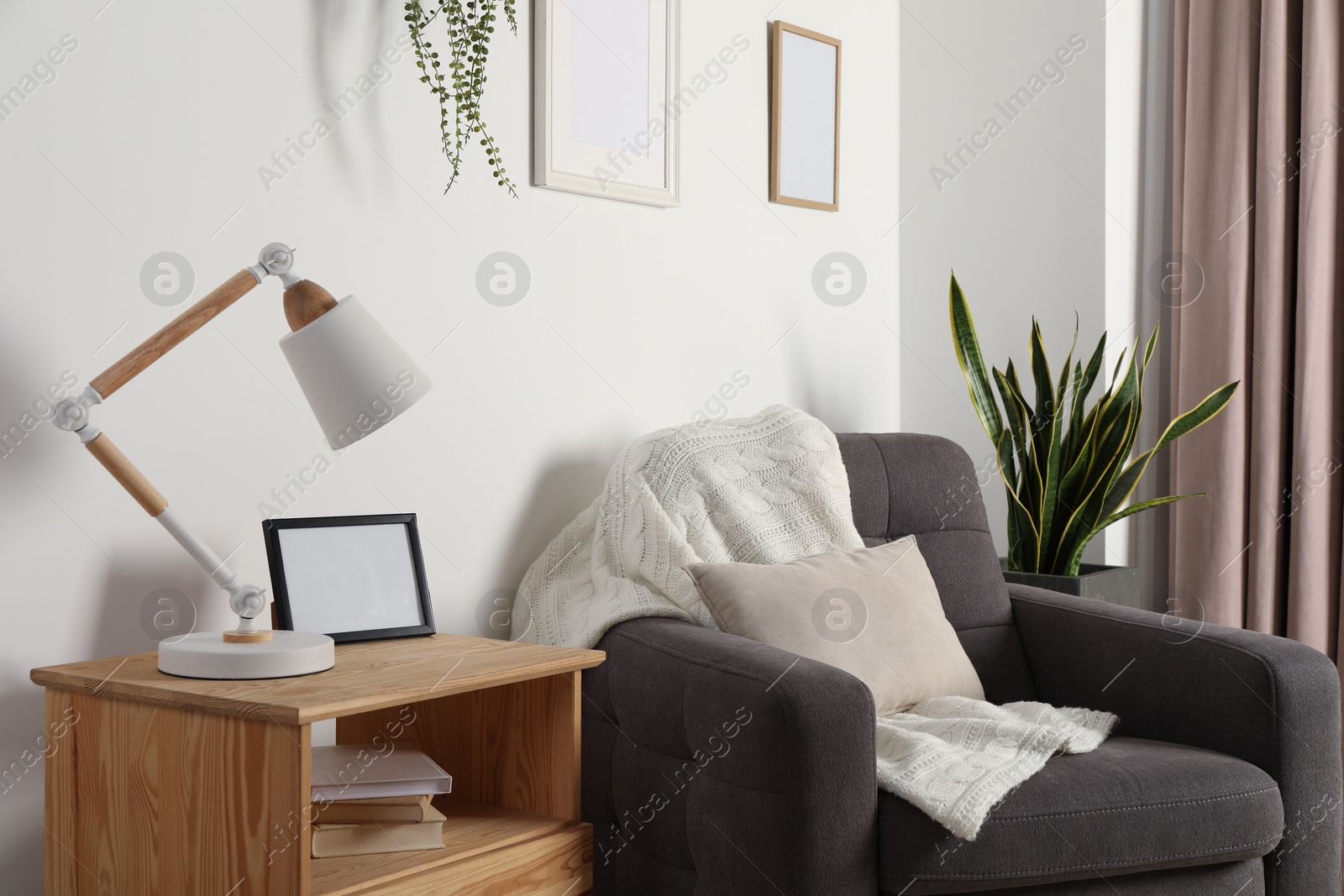 Photo of Stylish modern desk lamp and frame on wooden cabinet near armchair indoors