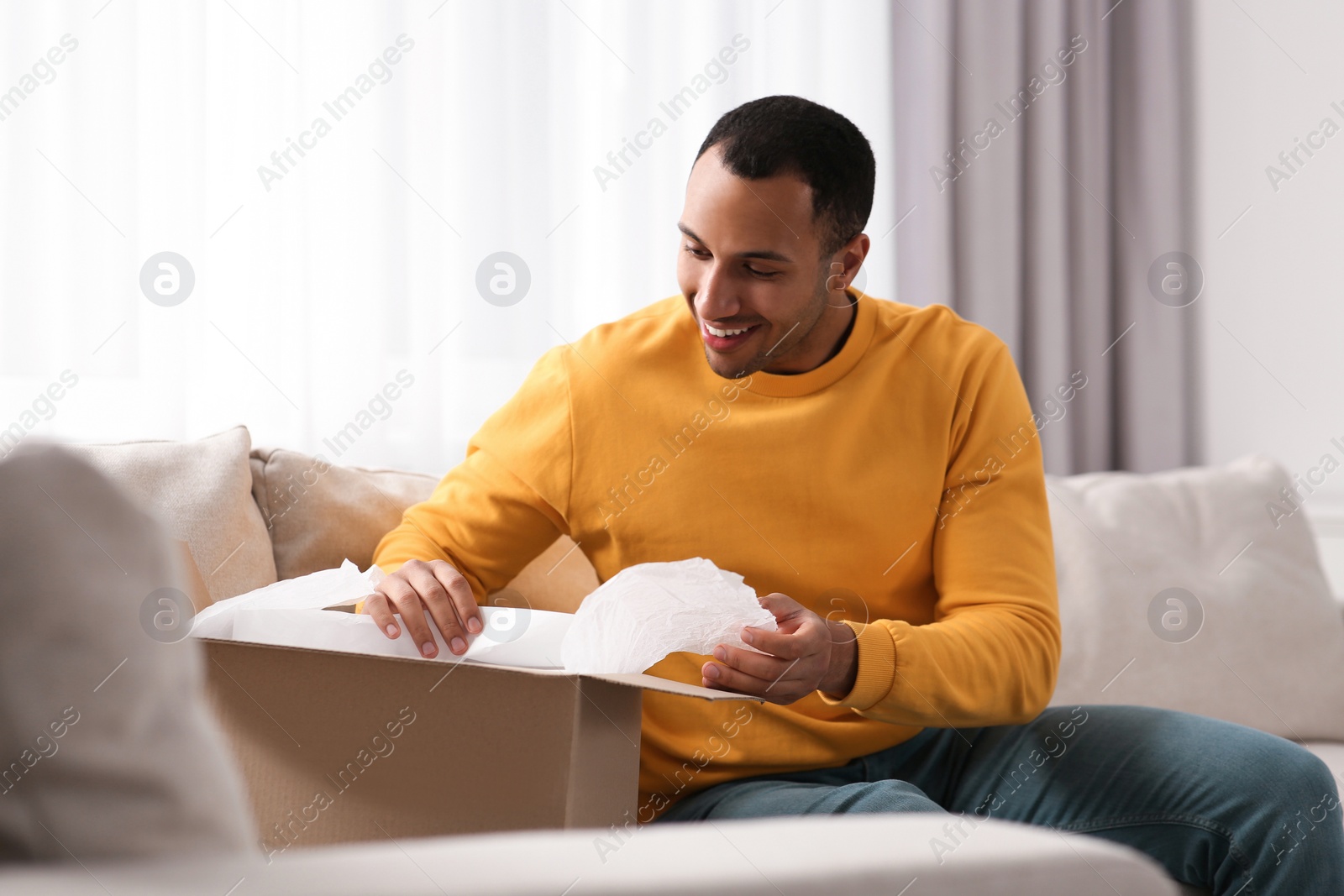 Photo of Happy young man opening parcel at home. Internet shopping