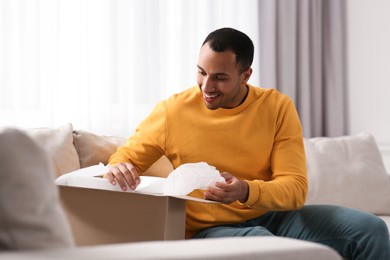 Photo of Happy young man opening parcel at home. Internet shopping