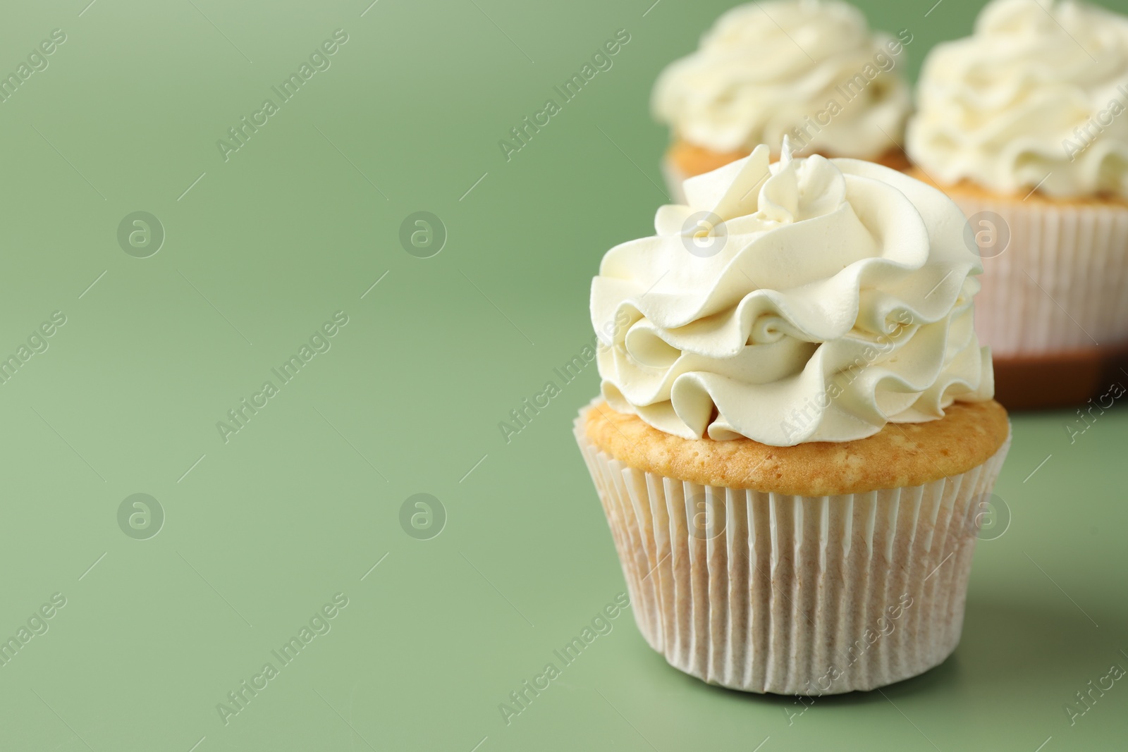 Photo of Tasty vanilla cupcakes with cream on green background, space for text