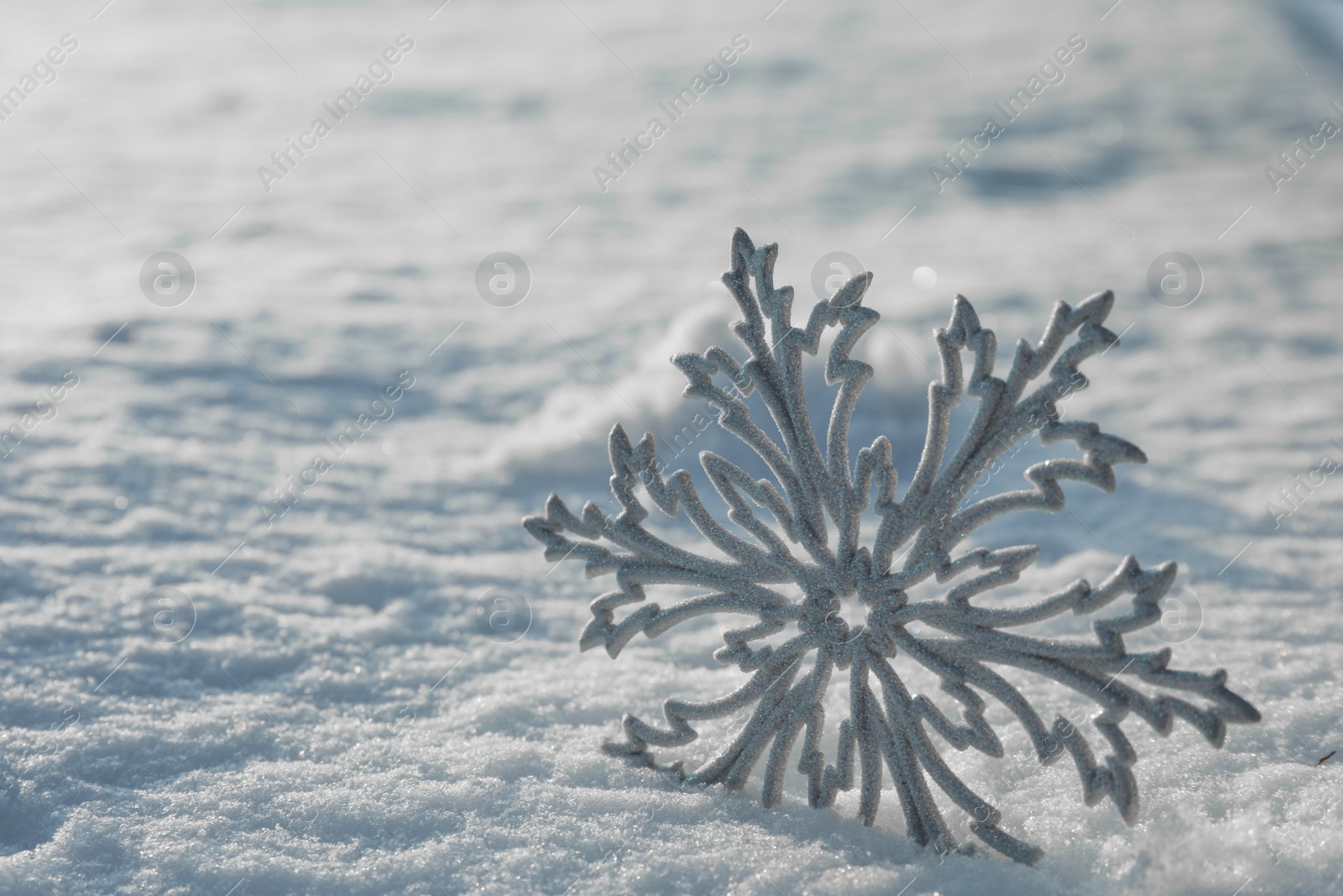 Photo of Beautiful decorative snowflake in white snow, outdoors. Space for text