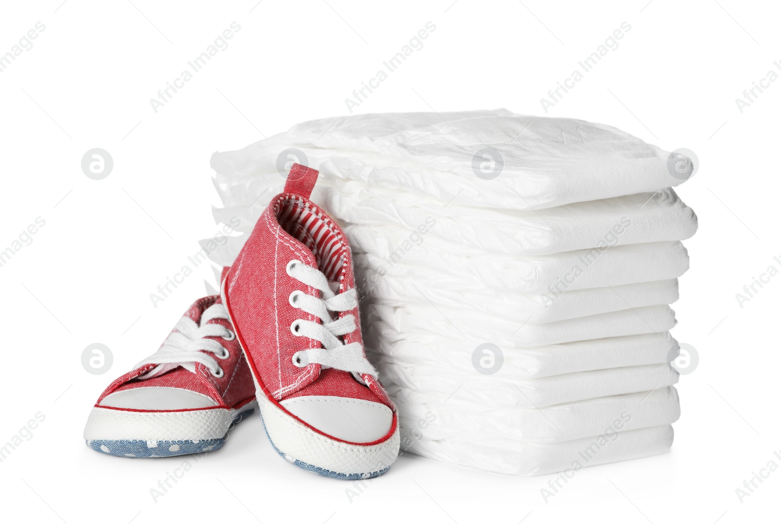 Photo of Stack of disposable diapers and child's shoes on white background