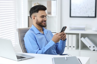 Photo of Happy young man using smartphone at white table in office