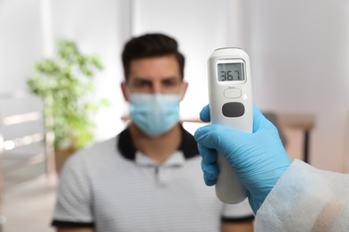 Photo of Doctor measuring man's temperature in office, closeup. Prevent spreading of Covid-19
