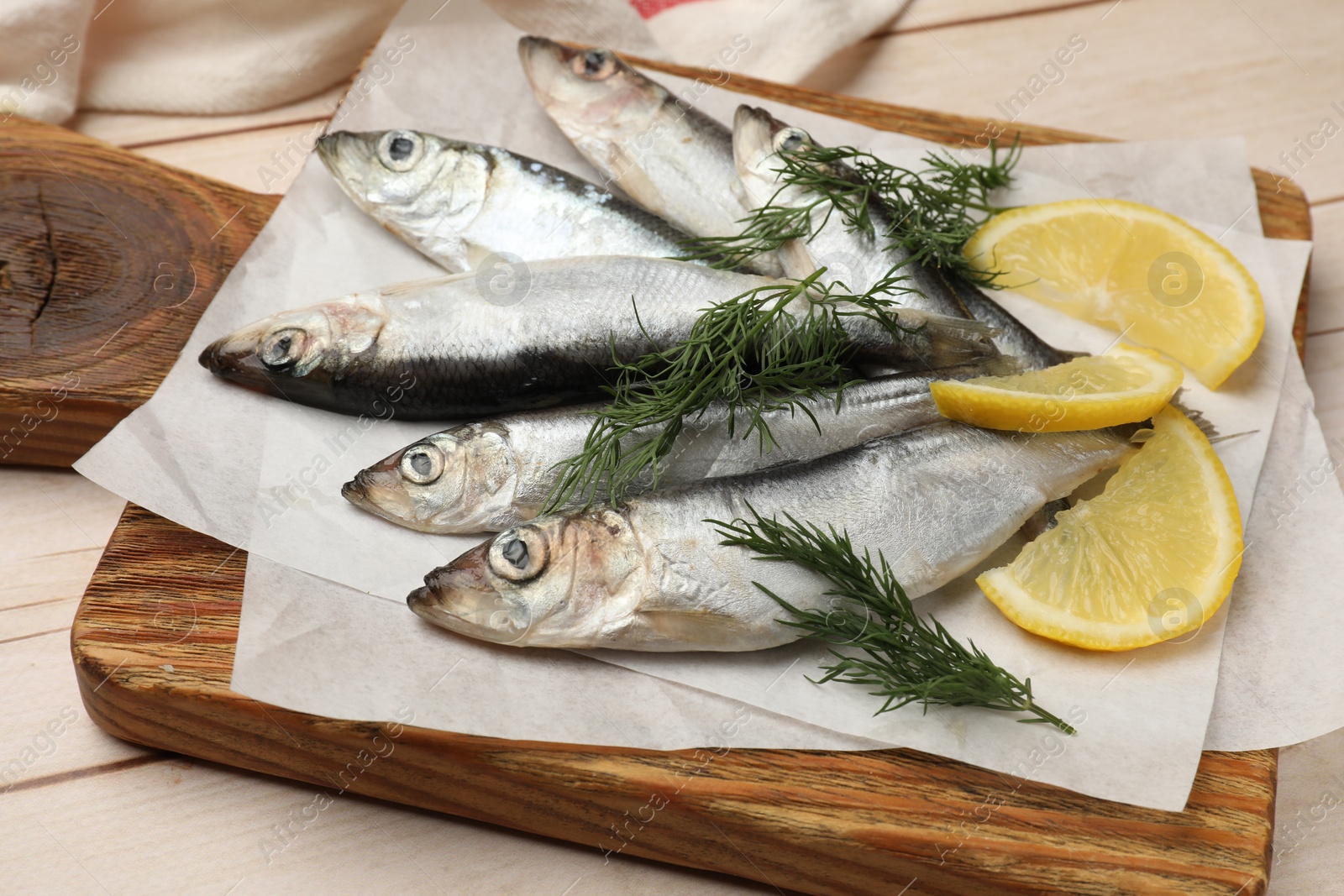 Photo of Fresh raw sprats, lemon and dill on light wooden table, closeup