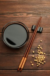 Photo of Soy sauce in bowl, soybeans and chopsticks on wooden table, flat lay