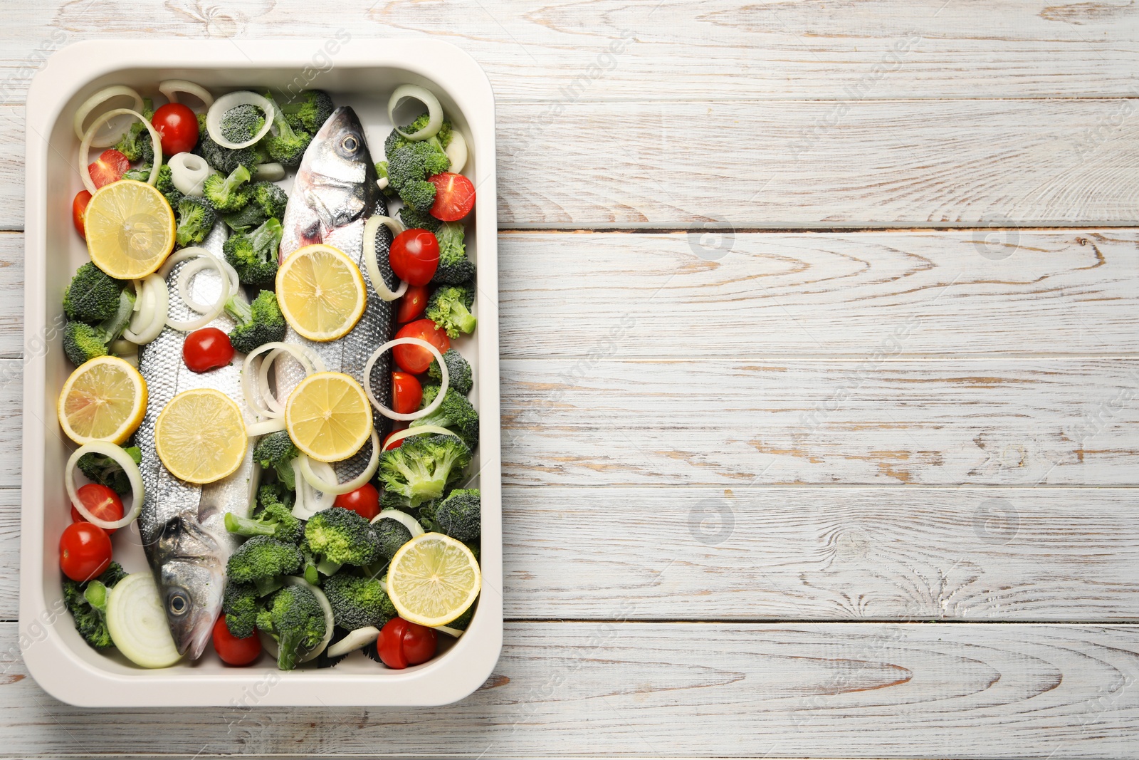 Photo of Raw fish with vegetables and lemon in baking dish on wooden table, top view. Space for text